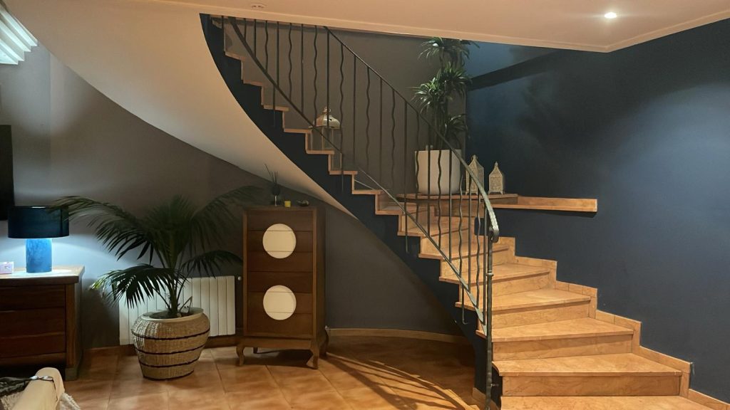 Escalera bovedada terminada en una vivienda, con peldaños cerámicos, barandilla de hierro forjado y diseño curvo, destacando un trabajo de reforma interior elegante y de alta calidad.